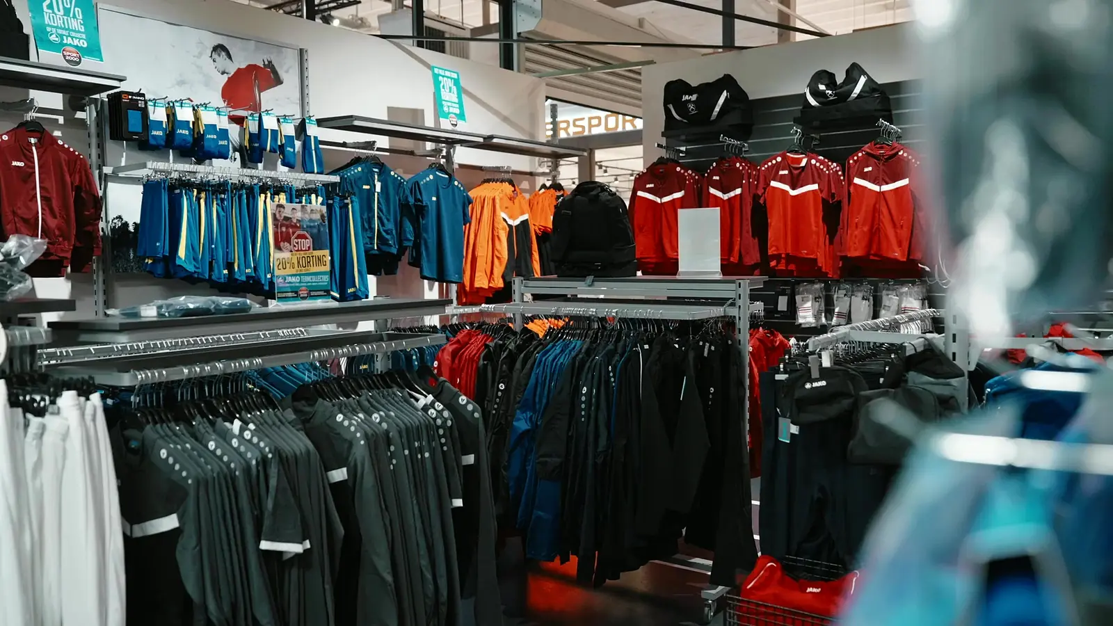 Rekken met JAKO-teamkleding in rood, blauw en oranje op de teamsportafdeling