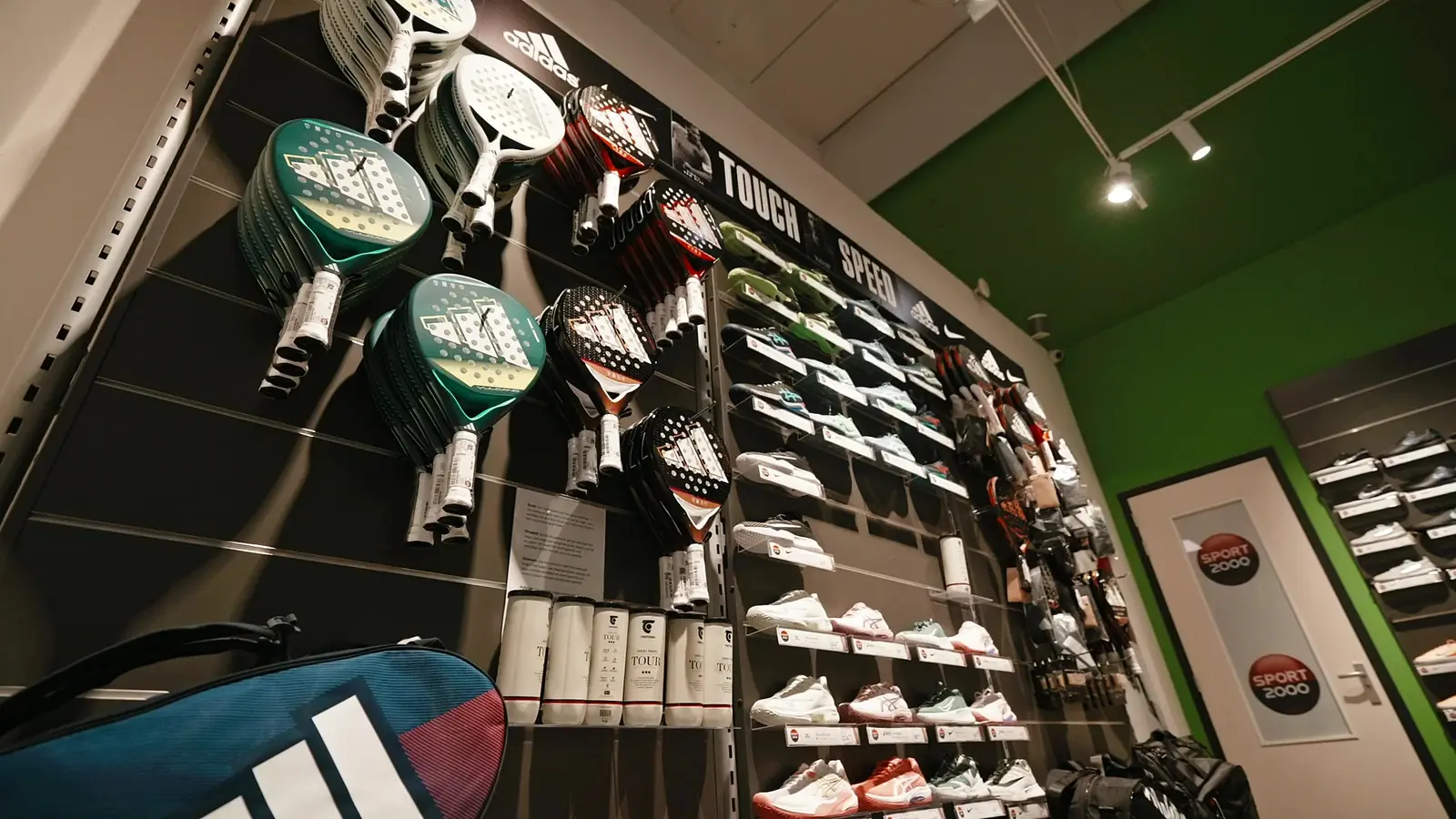 Padelwand met rackets, ballenkokers en tennisschoenen