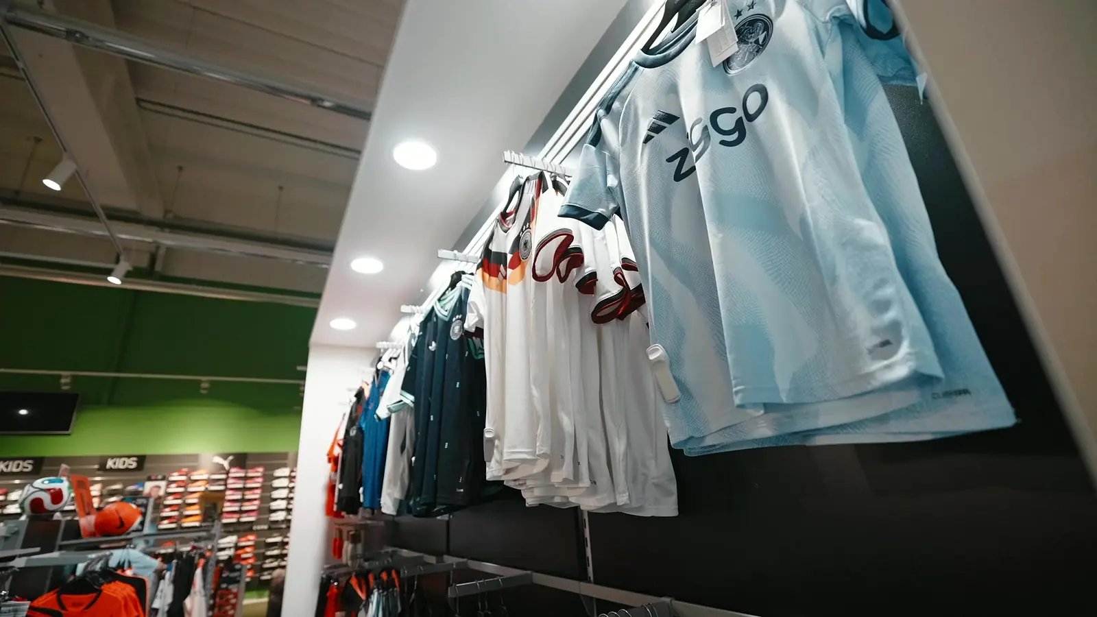 Rij clubshirts aan een rail, vooraan een lichtblauw uitshirt van Ajax